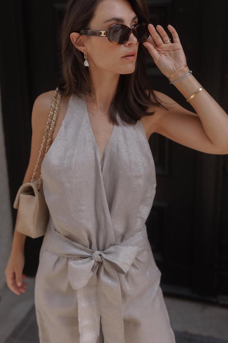 Woman in a shimmering silver-grey sleeveless jumpsuit with a tied waist bow.
