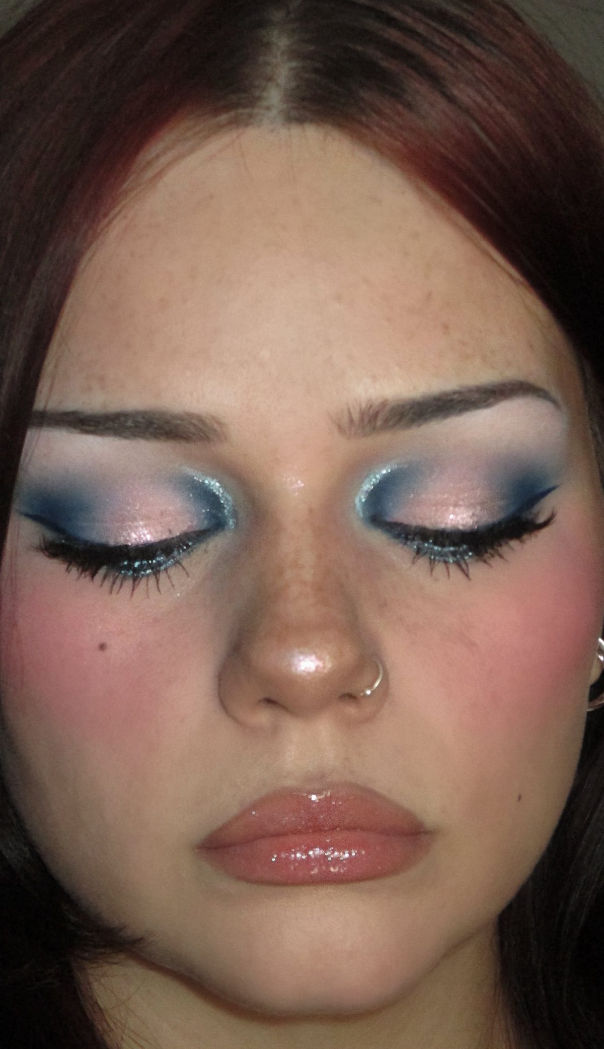 Person with blue and silver eyeshadow, winged eyeliner, and glossy pink lips.