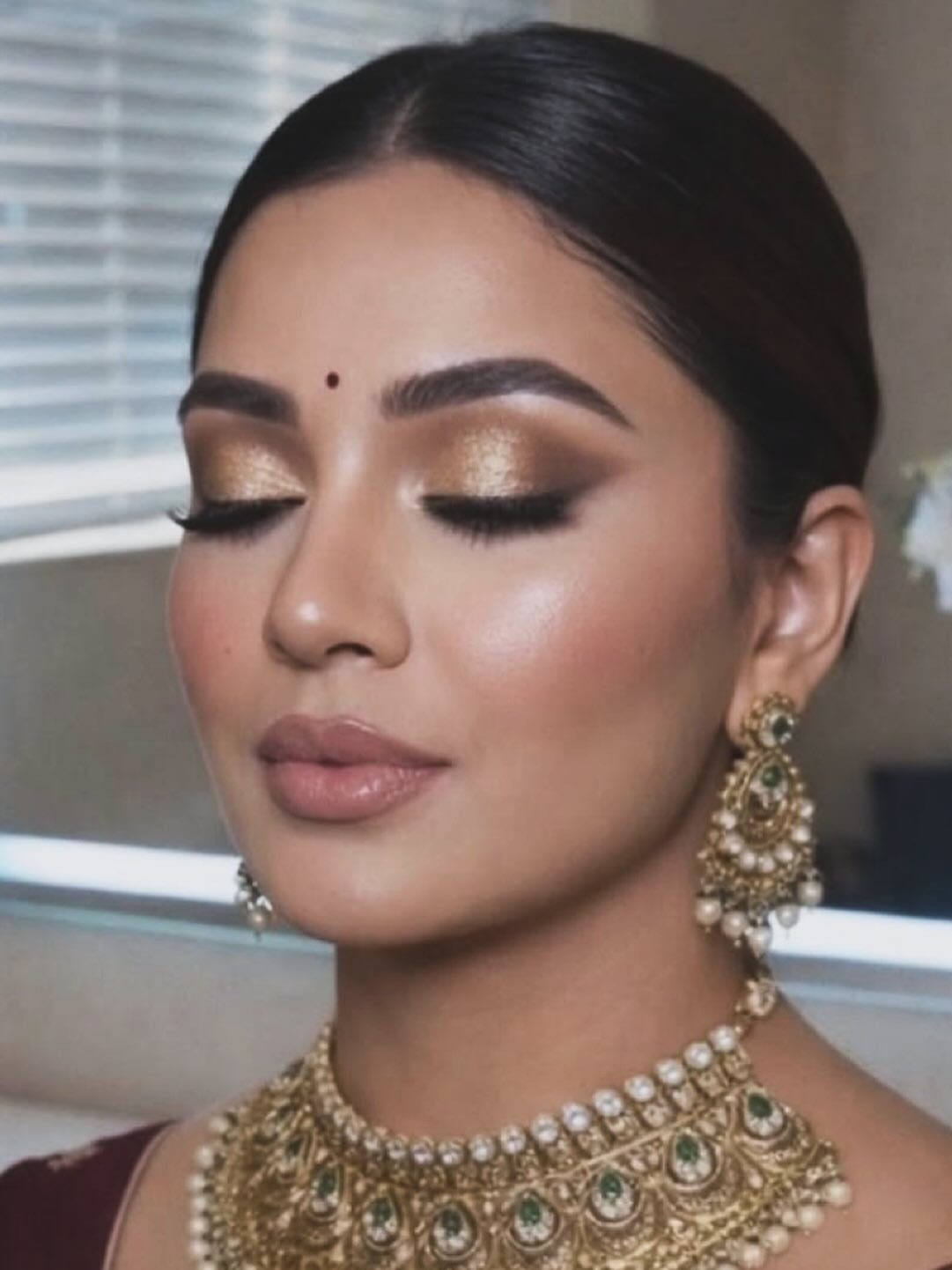 Woman with gold eyeshadow and contoured cheekbones wearing traditional gold and pearl jewelry.