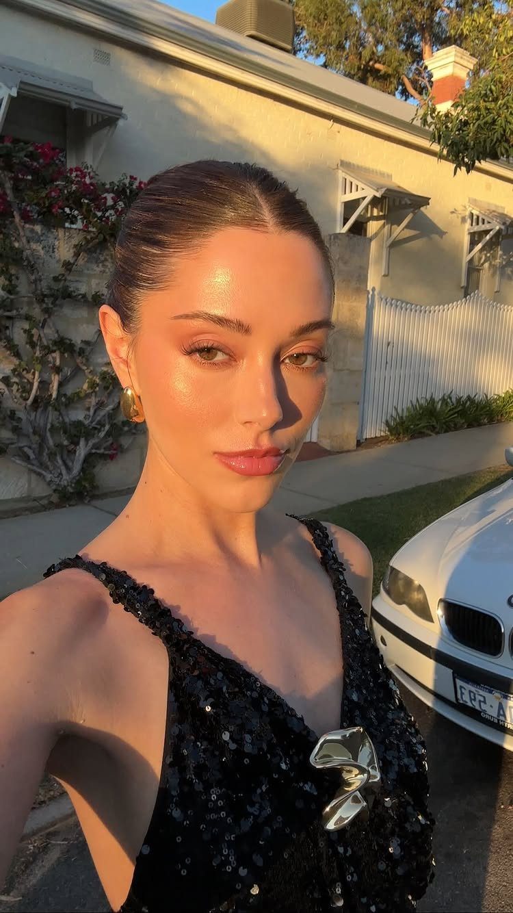 Woman with glowing skin and soft makeup wearing a black sequined dress outdoors.