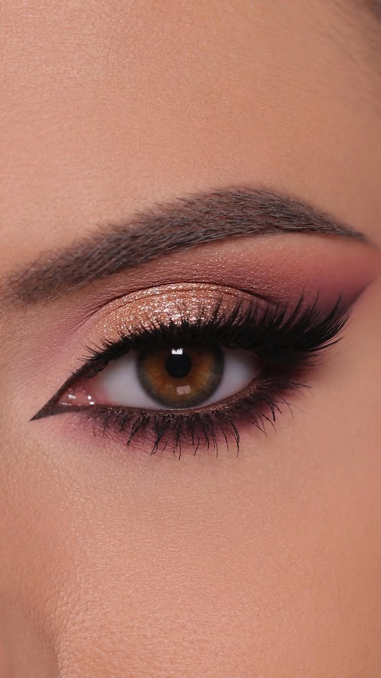 Eye with pink eyeshadow, gold glitter, winged eyeliner, and long voluminous lashes.