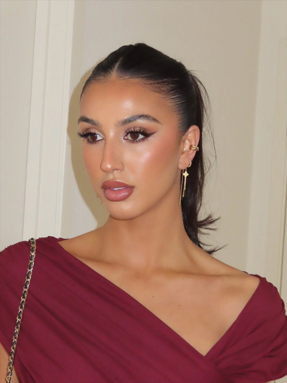 Woman with glowing highlighter on cheekbones and brow bones wearing a maroon dress.