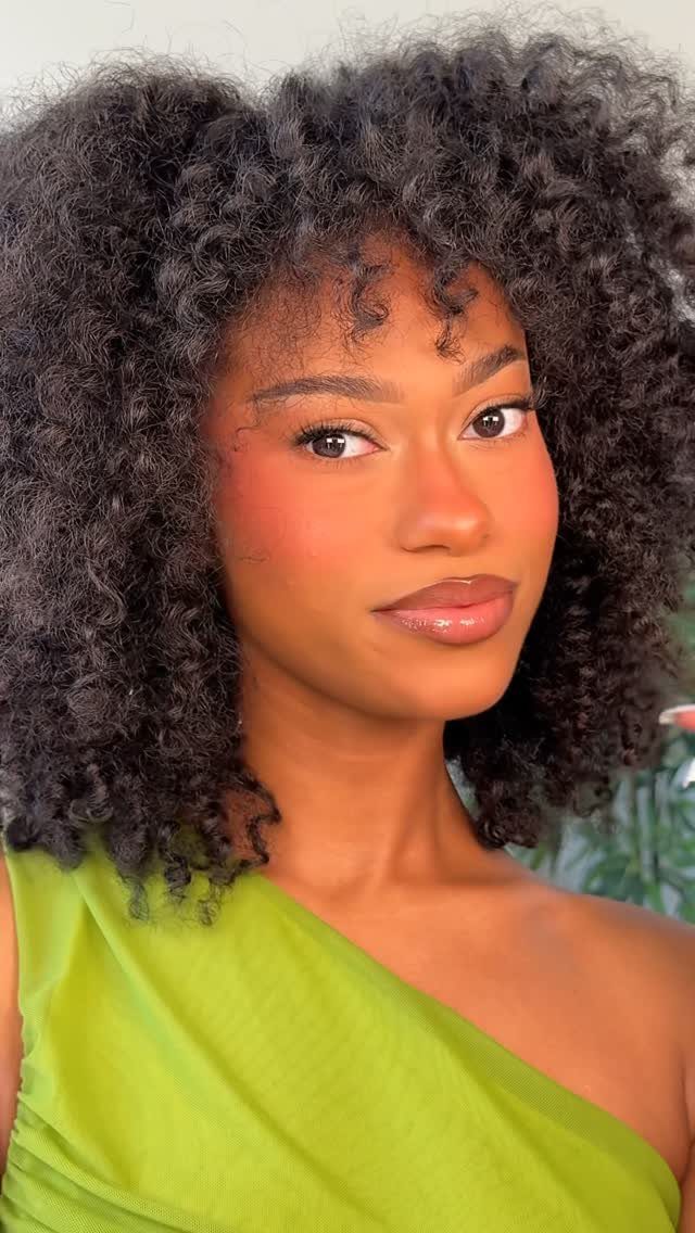 Woman with curly black hair wearing lime green top and warm-toned makeup.