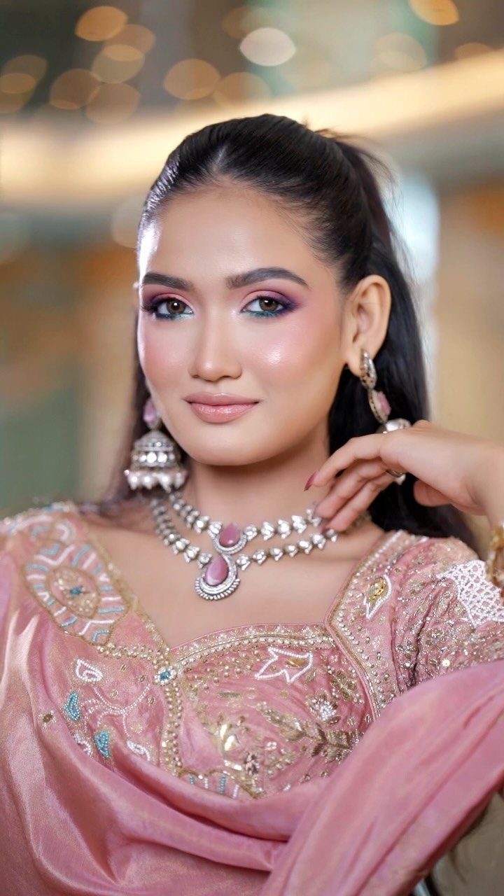 Woman with pink and purple eyeshadow wearing a pink embroidered traditional outfit and jewelry.