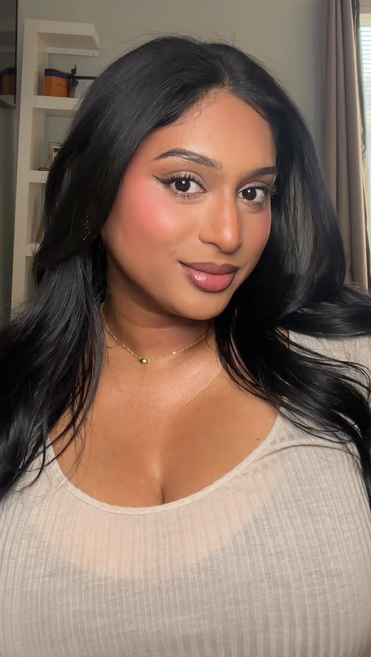 Woman with long black hair wearing soft glam makeup and a beige top.