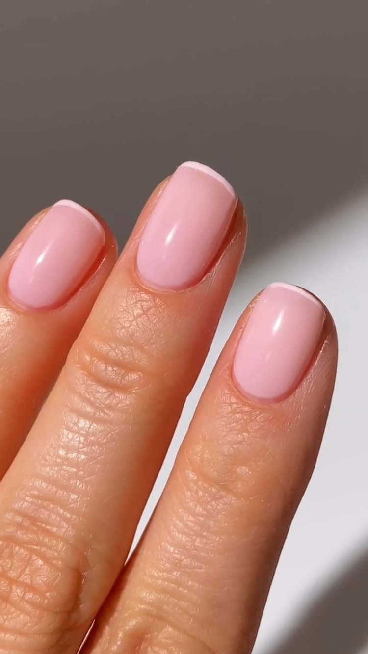 Light baby pink glossy nails on a person's fingers against a neutral background