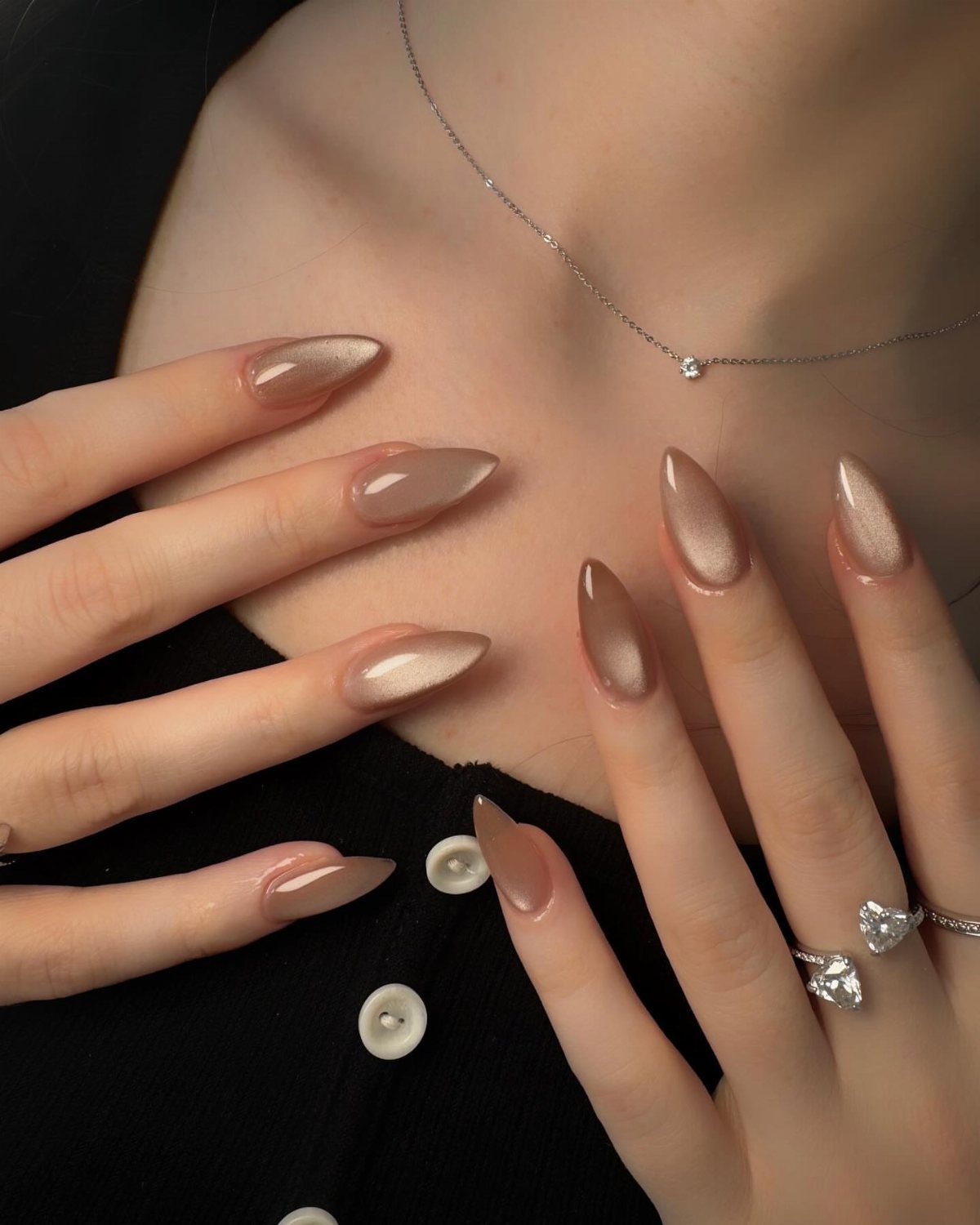 Champagne shimmer almond nails on a person wearing a black top and diamond jewelry.