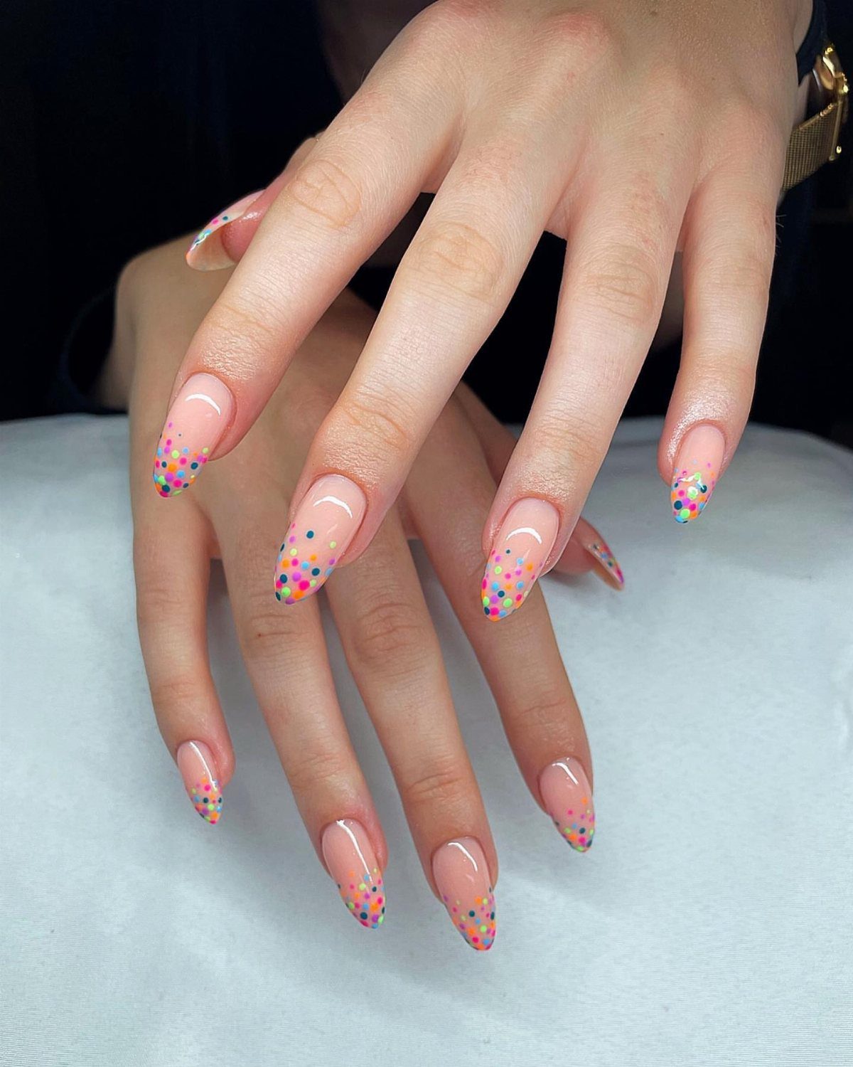 Almond-shaped nails with nude base and colorful confetti dots on the tips.
