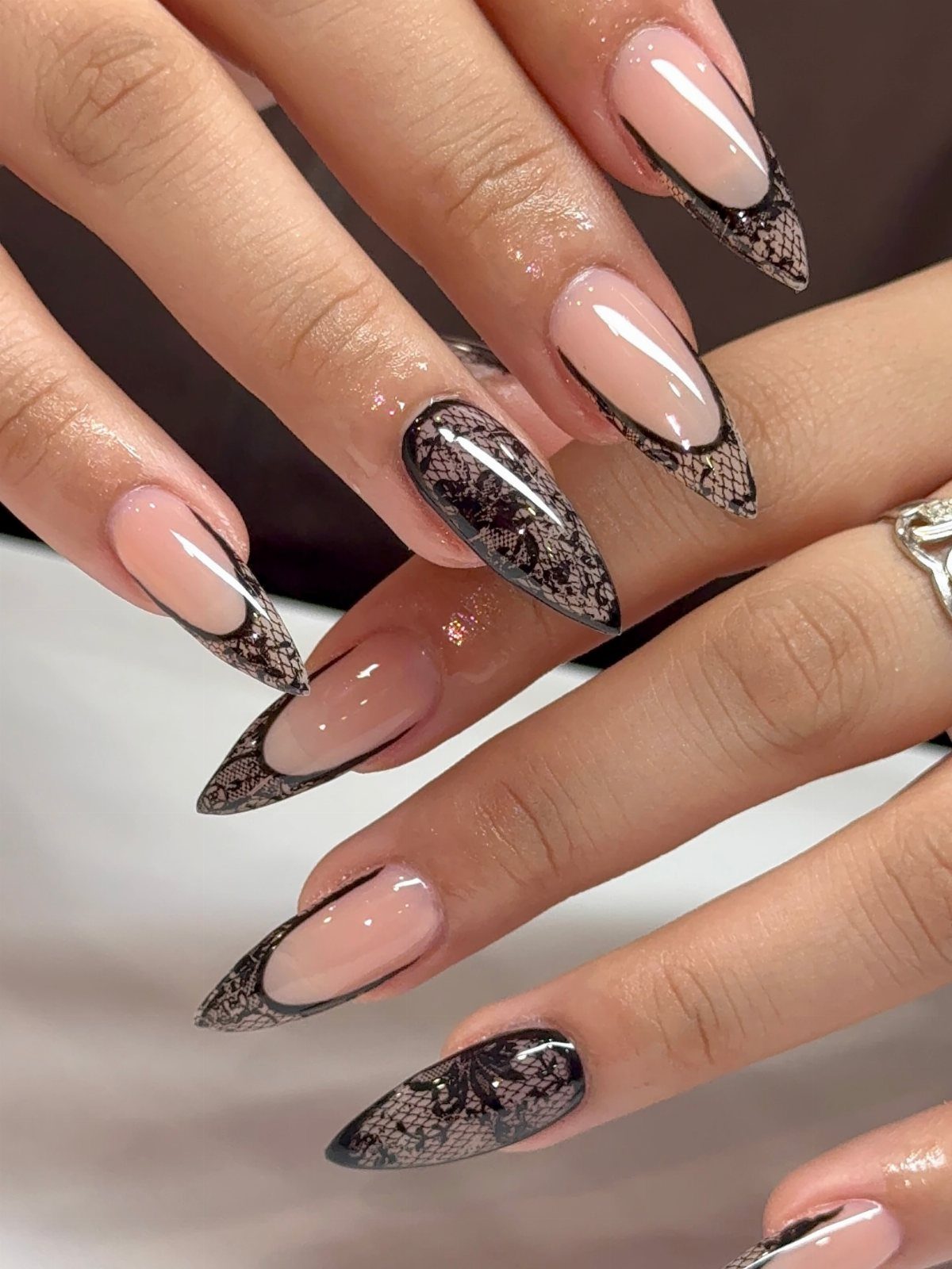 Almond-shaped nails with nude bases and black lace-patterned French tips.