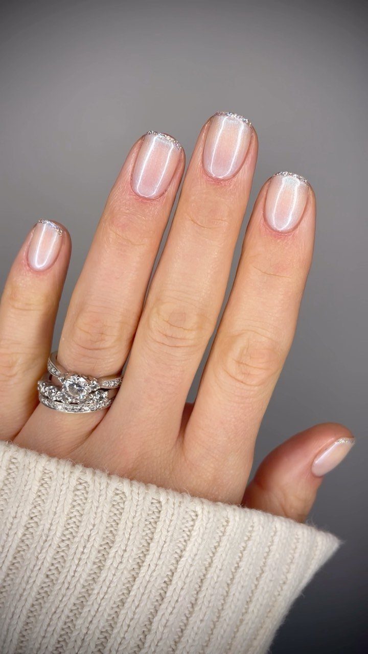 Hand with pale pink nails and thin shimmering silver micro-french tips and diamond rings