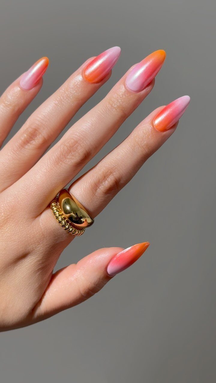 Almond-shaped nails with a pink to orange ombre gradient and gold rings.