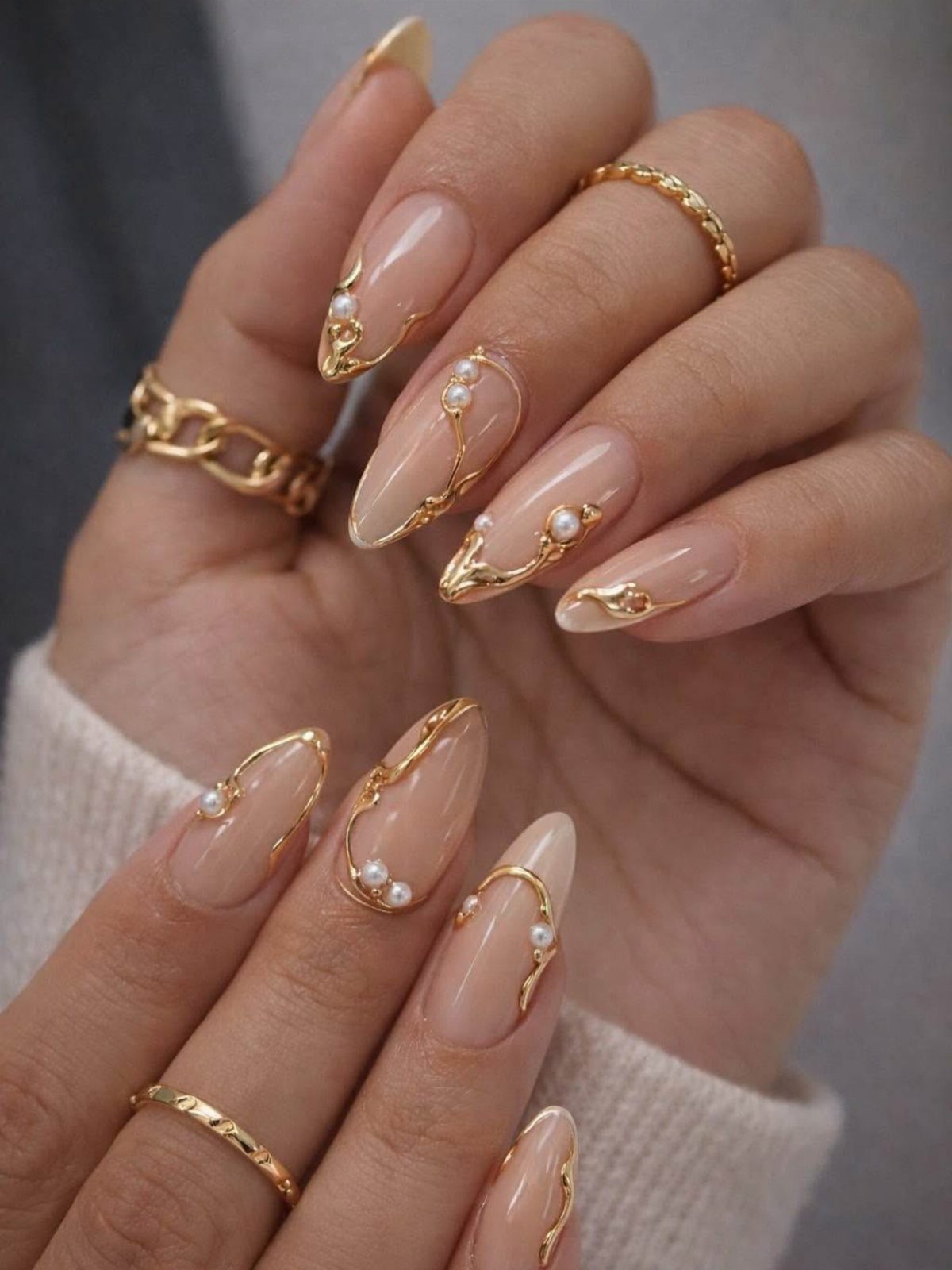 Nude almond nails with gold metallic swirls and small white pearl accents