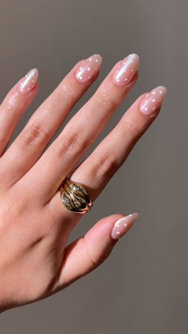 Almond-shaped pearlescent nails with white polka dots and a gold diamond ring.