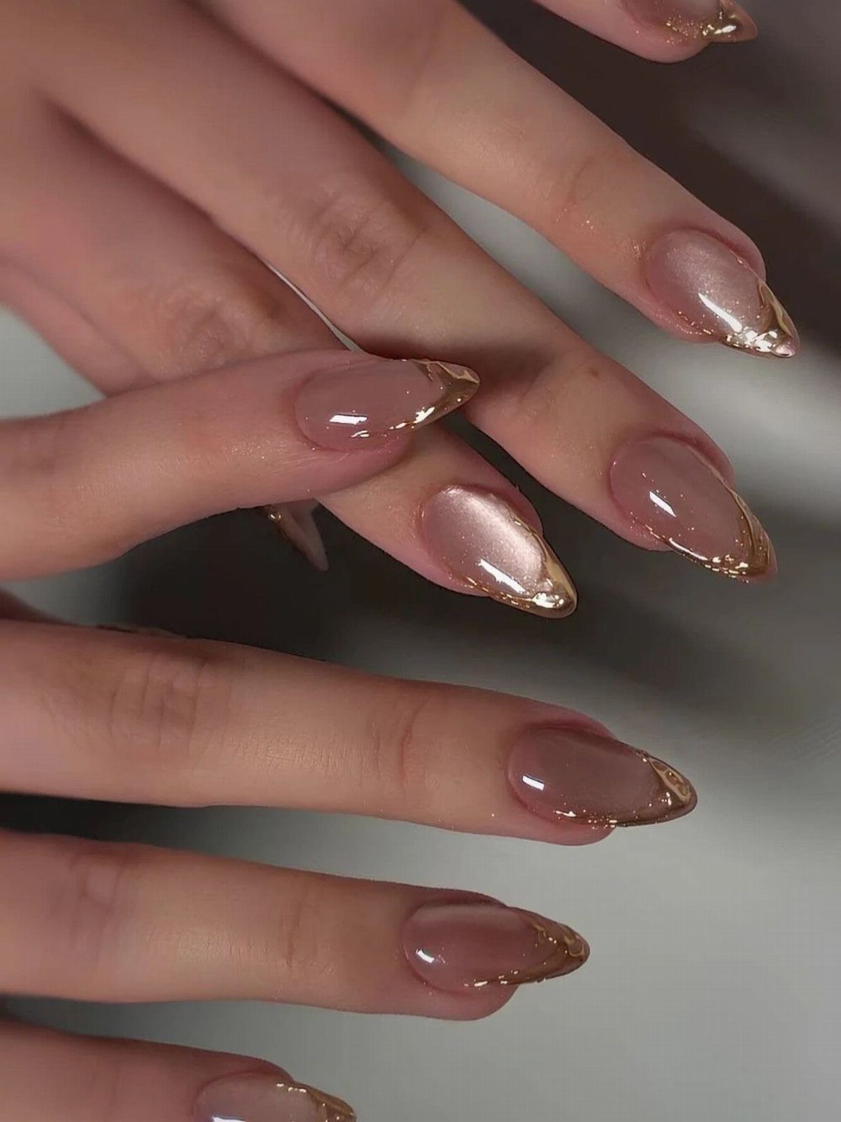 Almond shaped nails with pearlescent nude polish and metallic gold chrome tips.