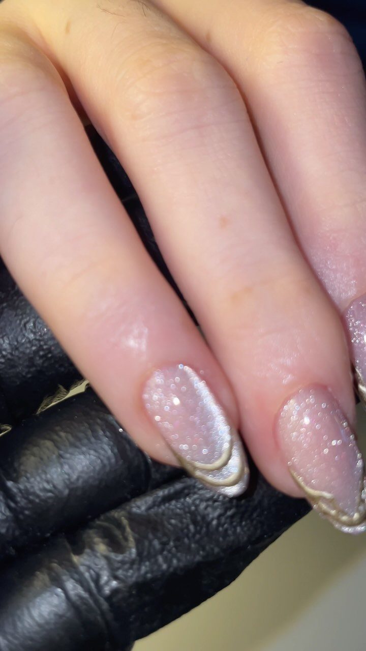 Oval nails with silver glitter and gold swirling line art accents on the tips.