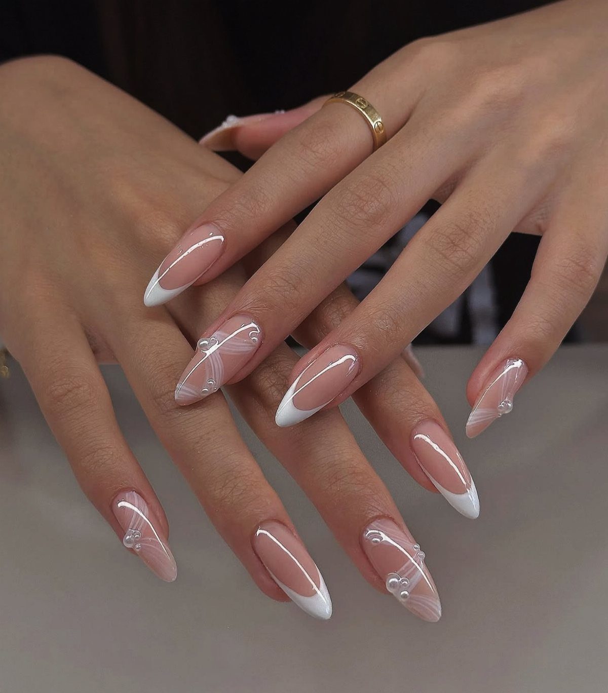 Almond-shaped nails with white French tips and delicate white swirl patterns and pearls.