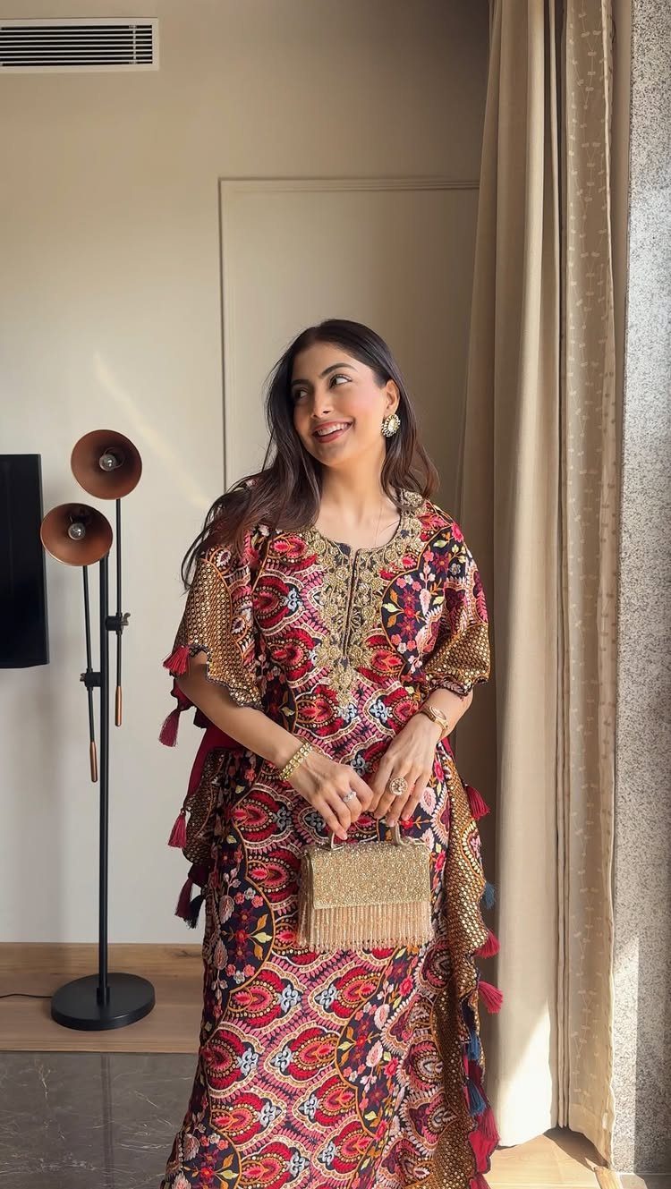 Woman in a red and gold patterned kaftan holding a gold fringed handbag.