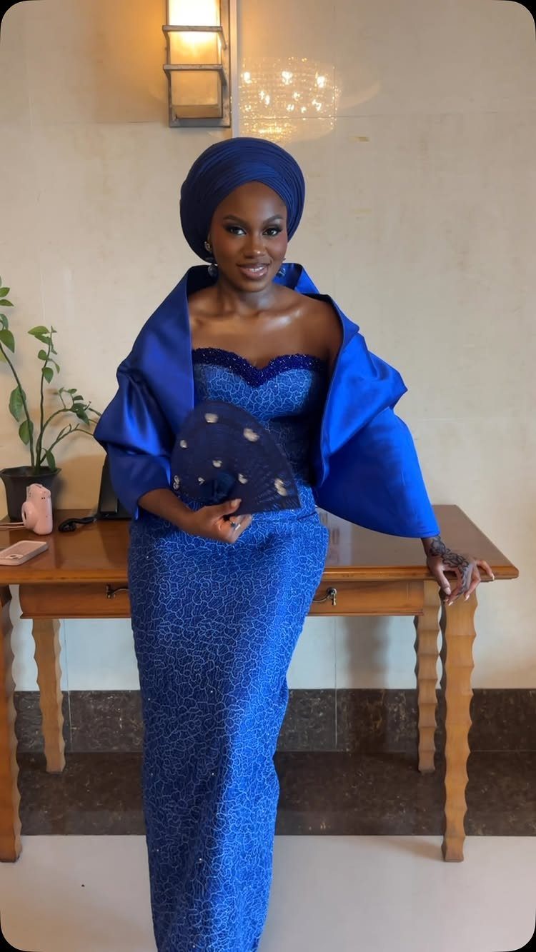 Woman in royal blue textured gown and gele head tie posing indoors.