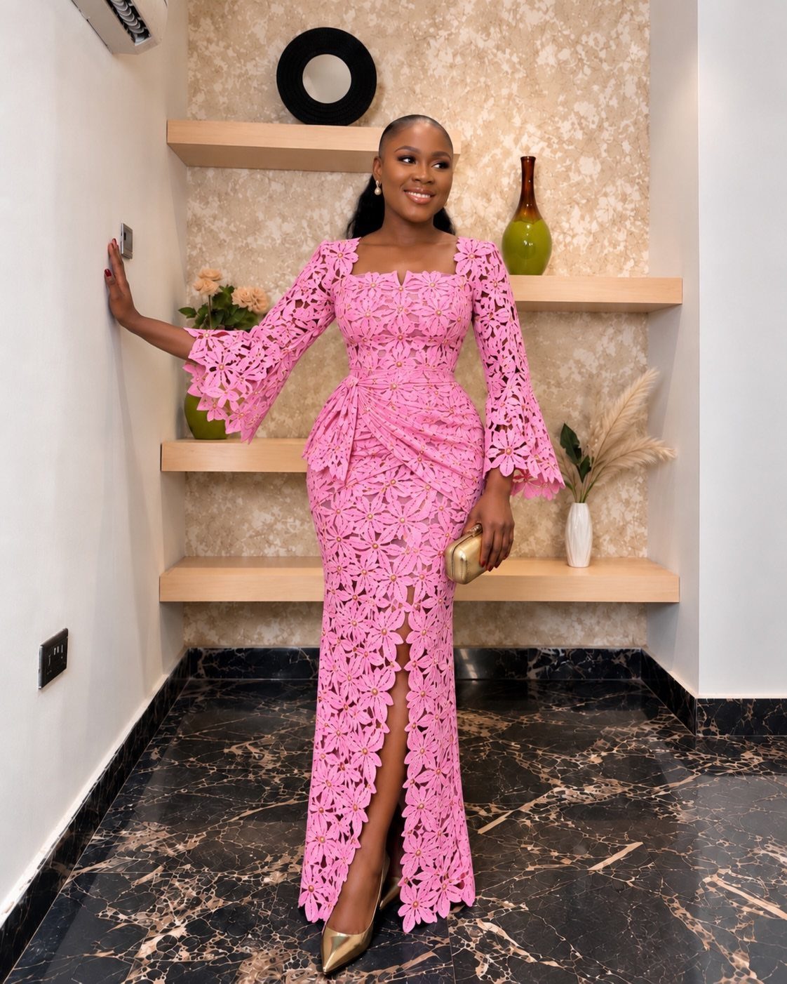 Woman in a pink lace maxi dress with bell sleeves and a gold clutch.