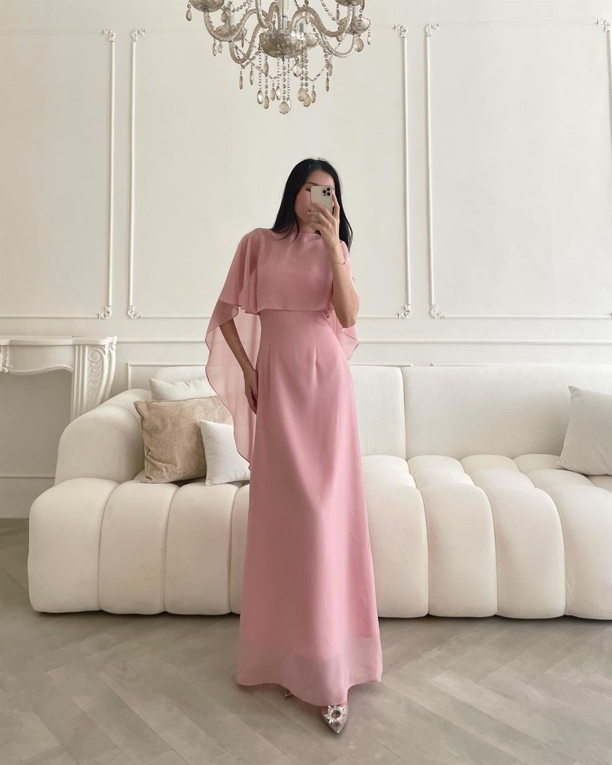 Woman in a long pink cape dress posing in a white living room