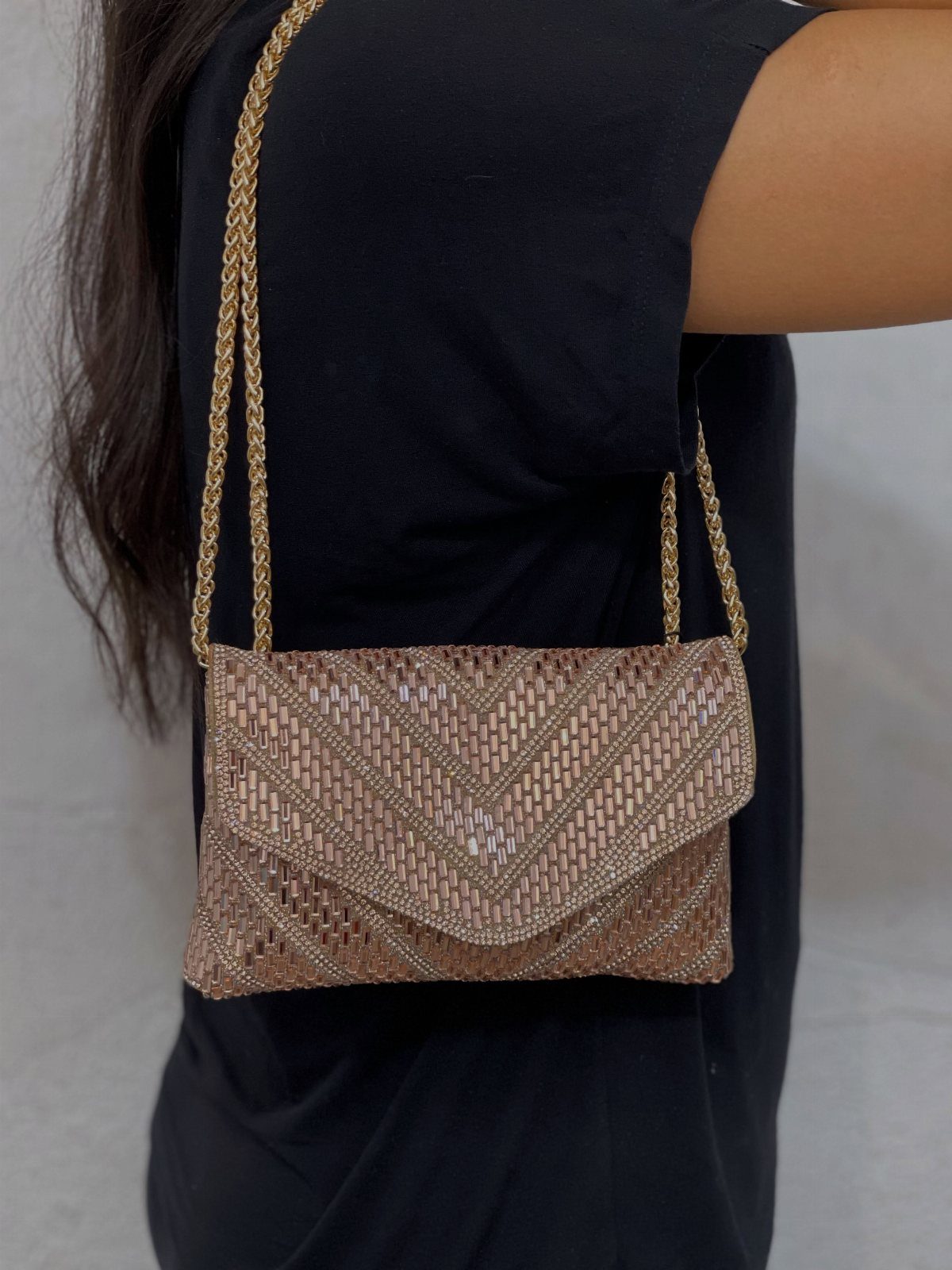 Rose-gold beaded clutch purse with gold chain strap worn over a black shirt.