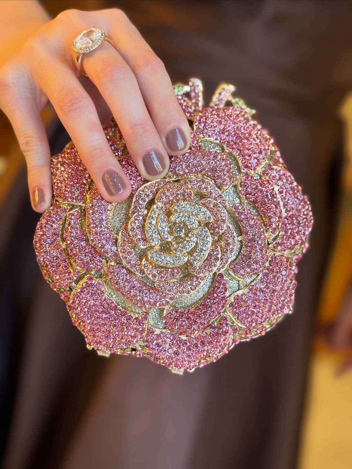 Pink rose-shaped crystal clutch bag held by a hand with a diamond ring.
