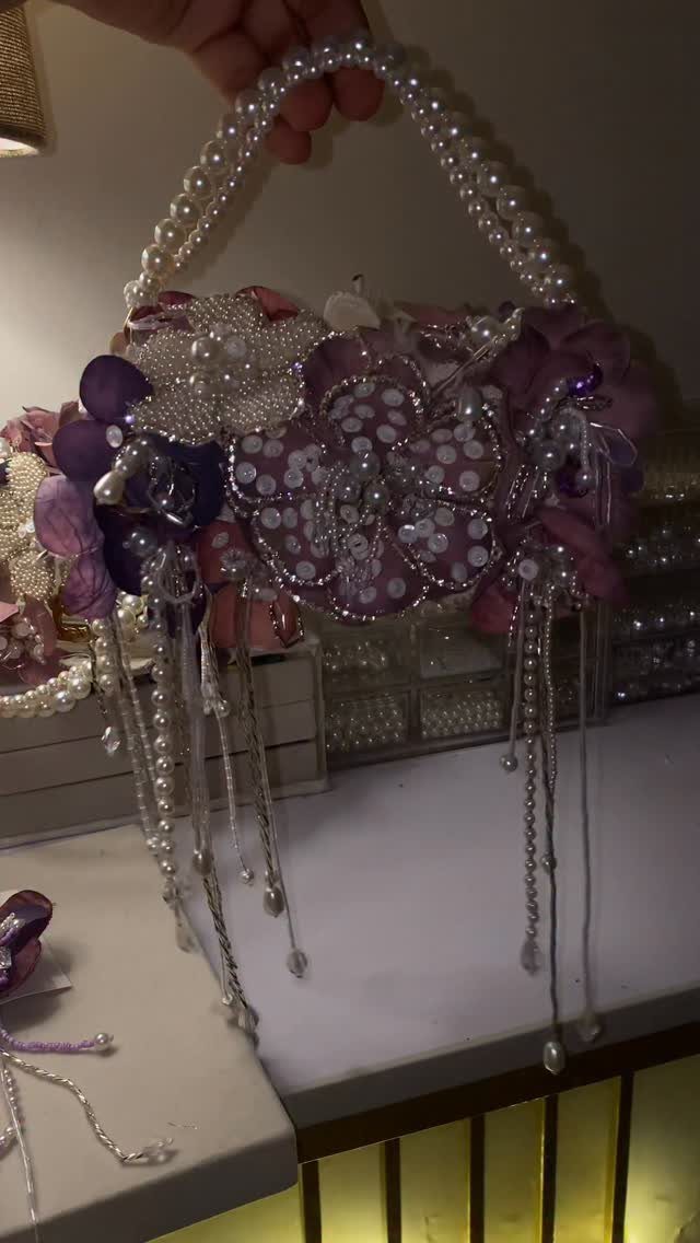 Purple floral handbag with pearl handle and dangling pearl beads held by a hand.