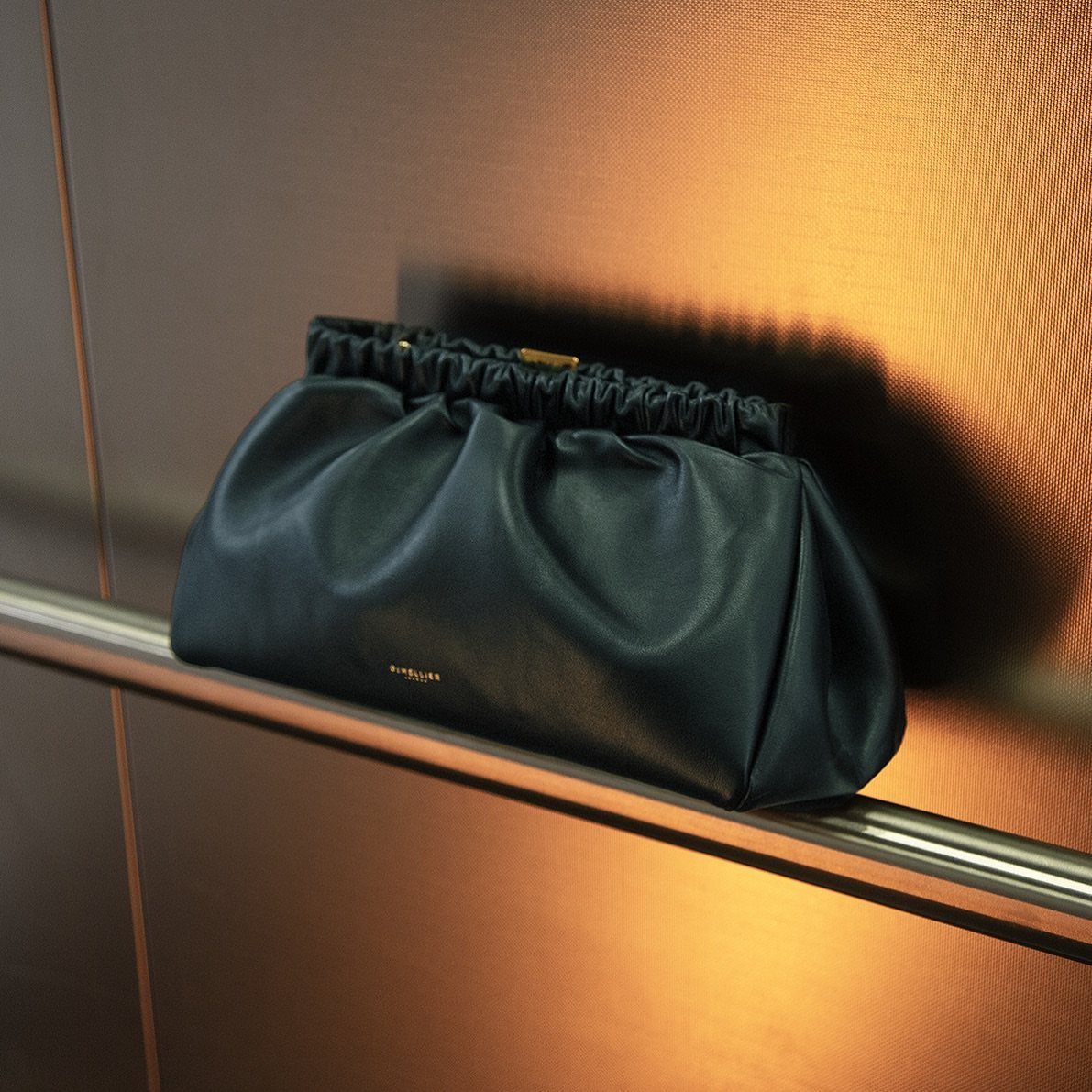 Dark navy blue leather clutch bag resting on a silver metal railing.