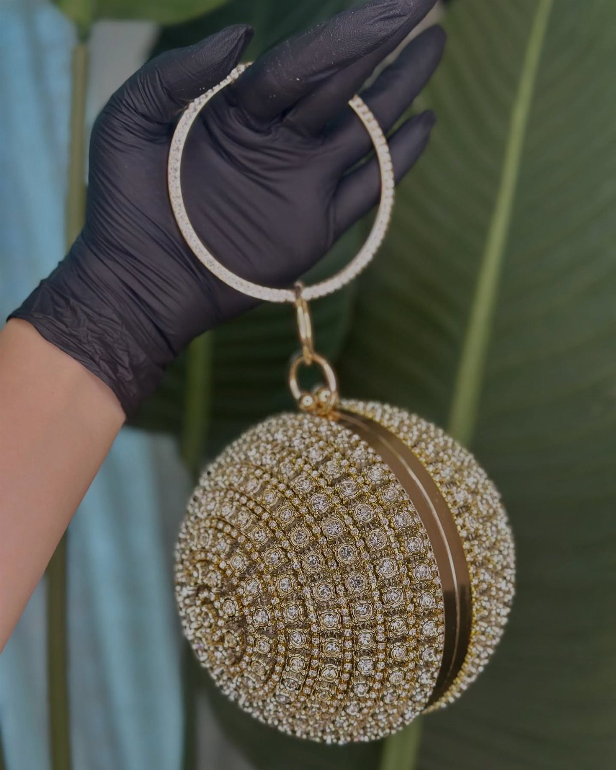 Spherical gold crystal clutch bag with a circular handle held by a gloved hand.