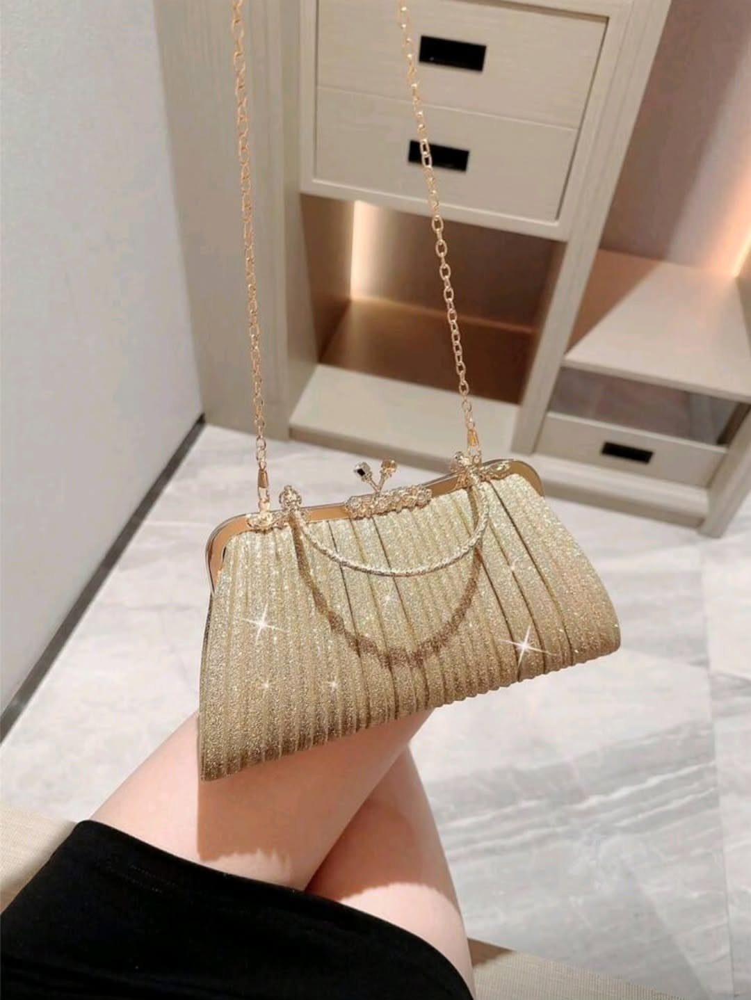 Gold glittery clutch purse with a chain strap held against a black dress.