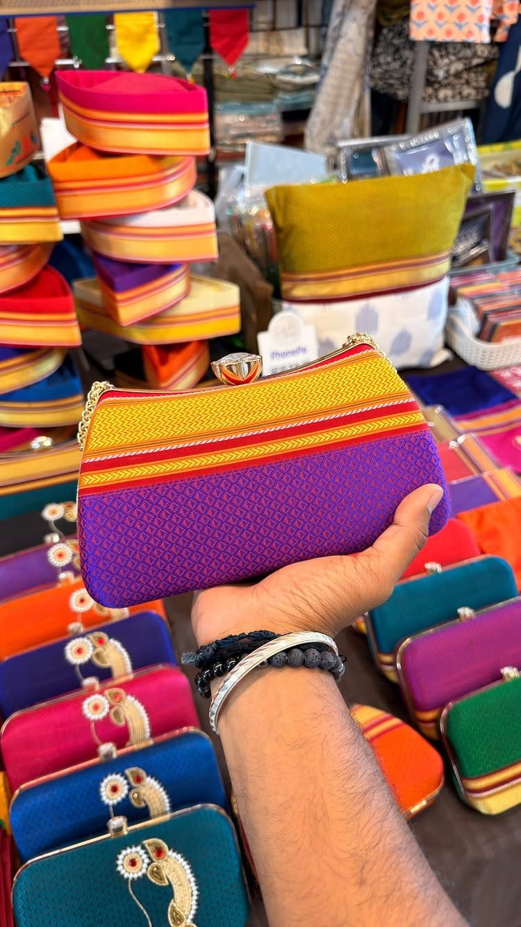 Colorful striped fabric pouch with a metal clasp held in a hand.