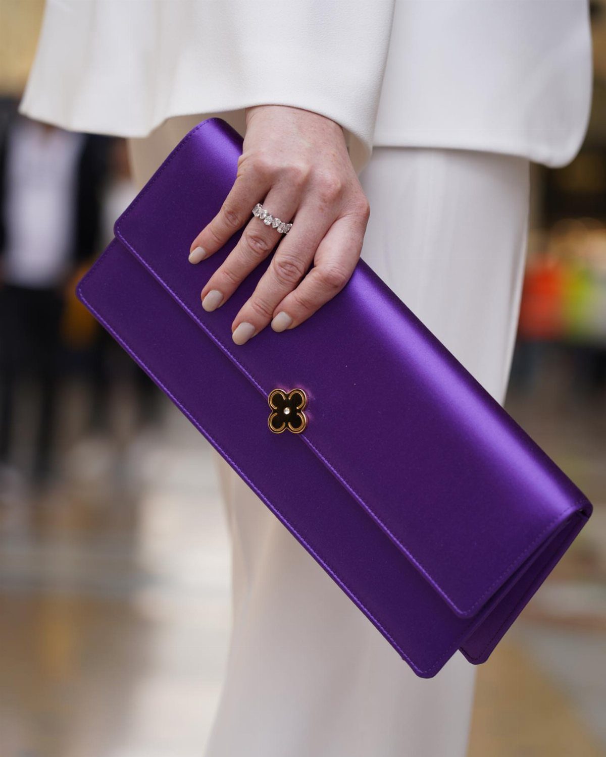 Purple satin clutch with gold flower clasp held by person in white clothing
