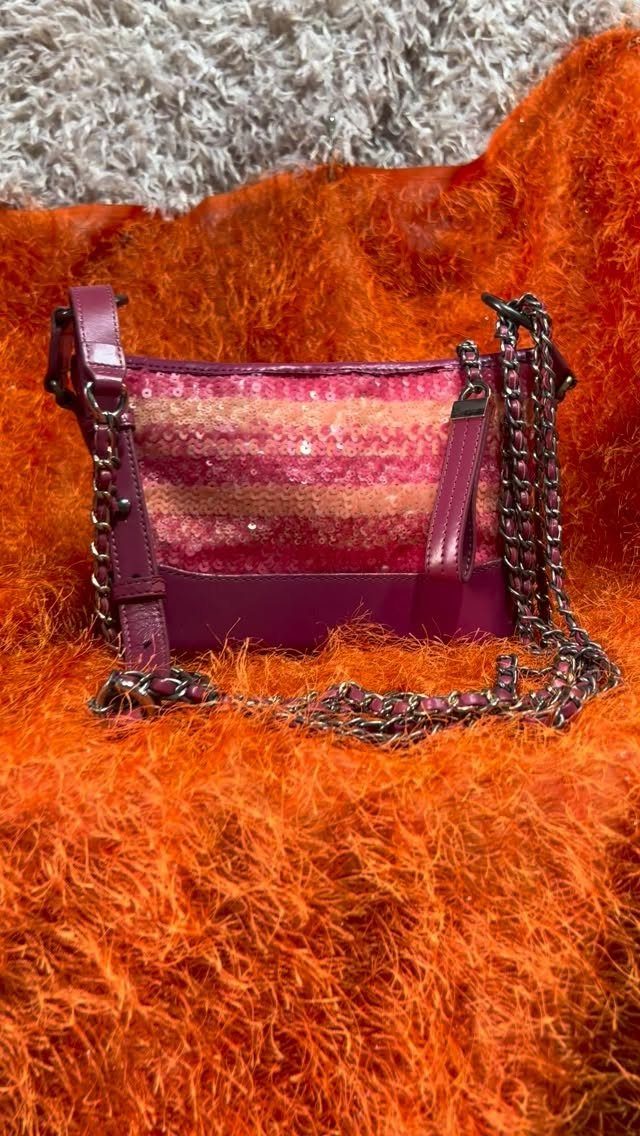 Purple and pink sequined crossbody bag with chain strap on orange shaggy fur.