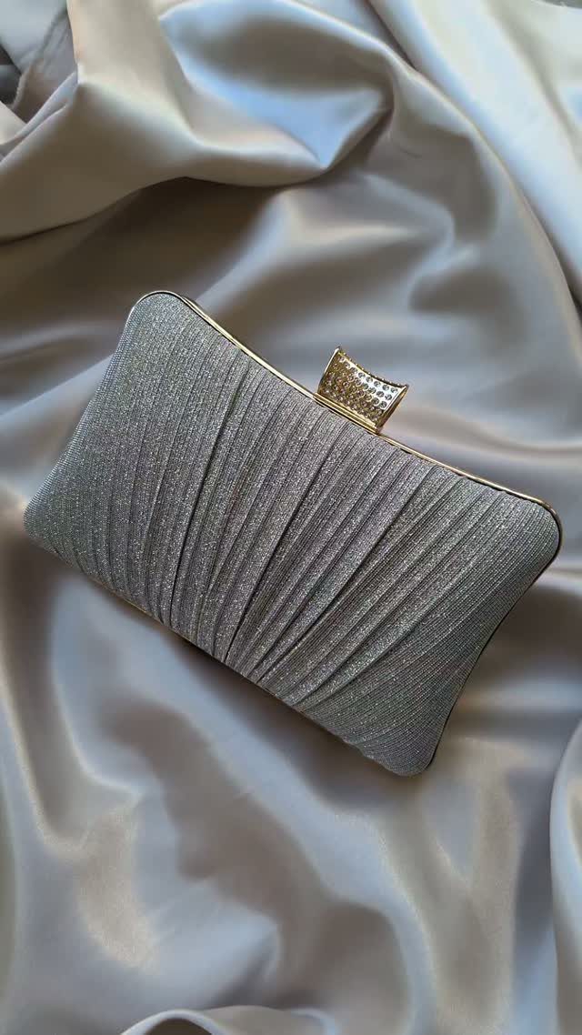 Silver glittery pleated clutch purse resting on draped champagne satin fabric