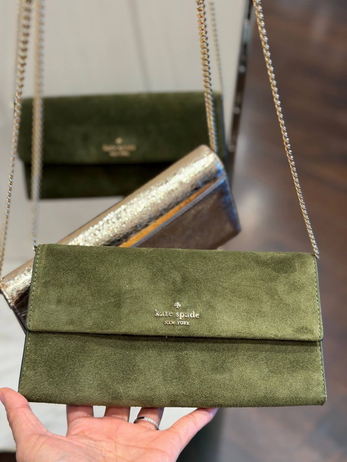 Olive green suede clutch purse with gold chain strap held by a hand