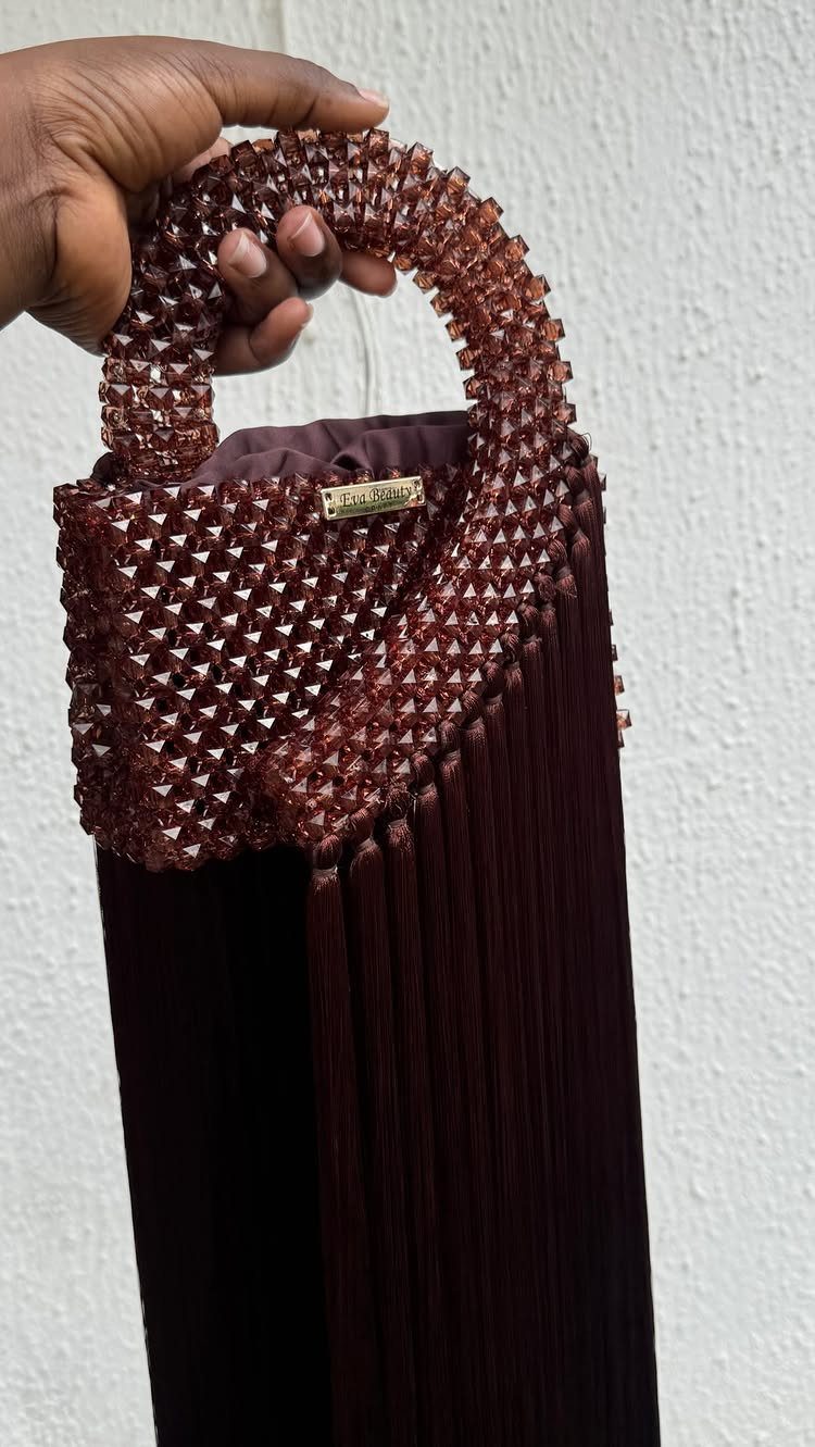 Burgundy beaded purse with a circular handle and long fringe held by a hand.