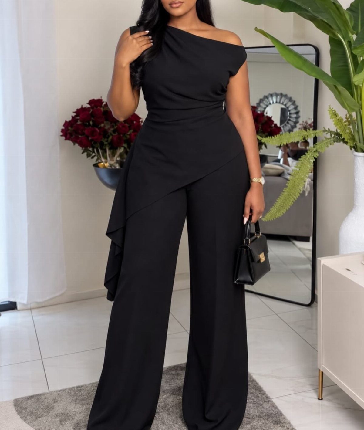 Woman in a one-shoulder black wide-leg jumpsuit holding a small black handbag.