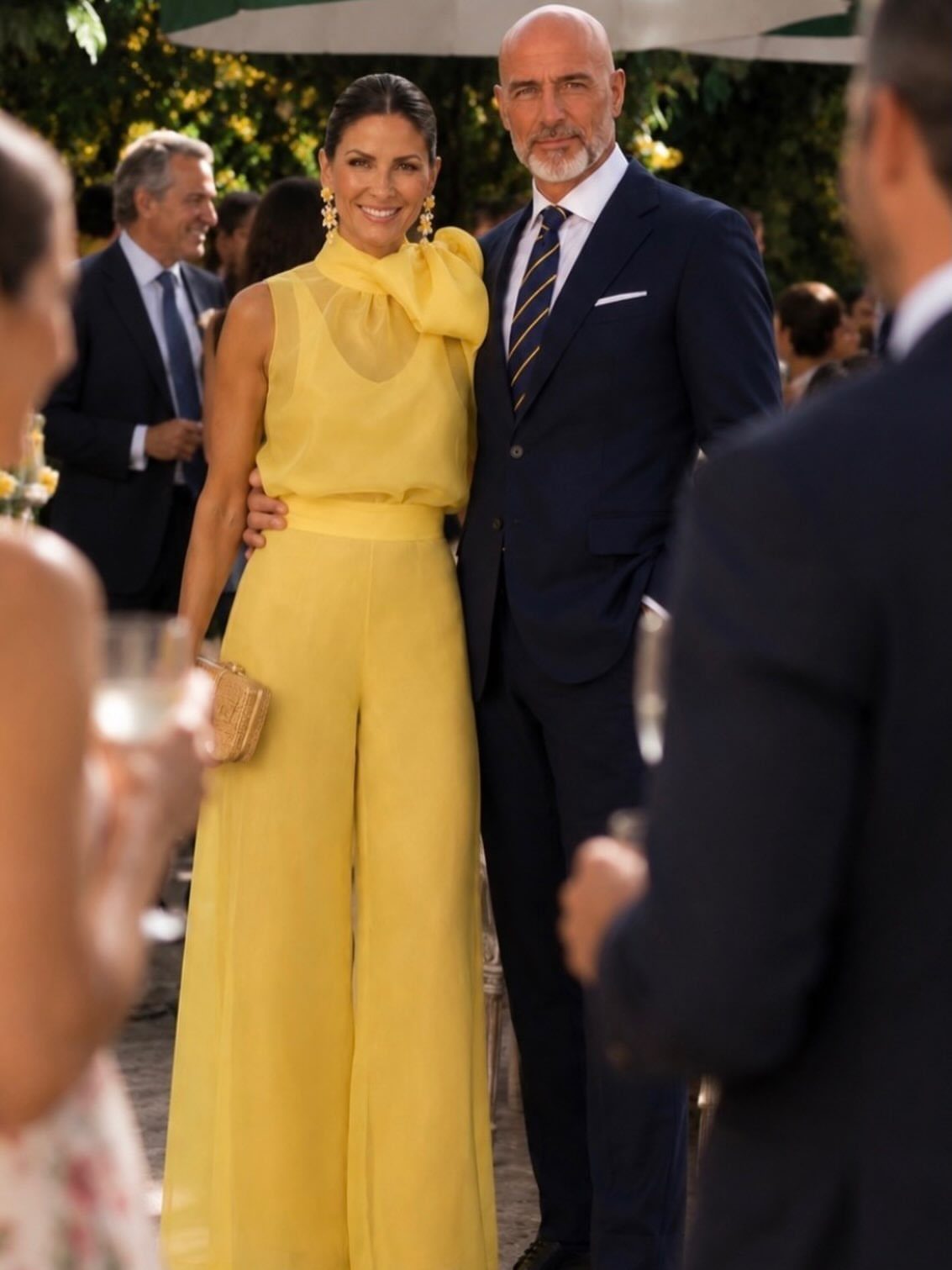 Woman in a yellow wide-leg jumpsuit standing with a man in a navy suit.
