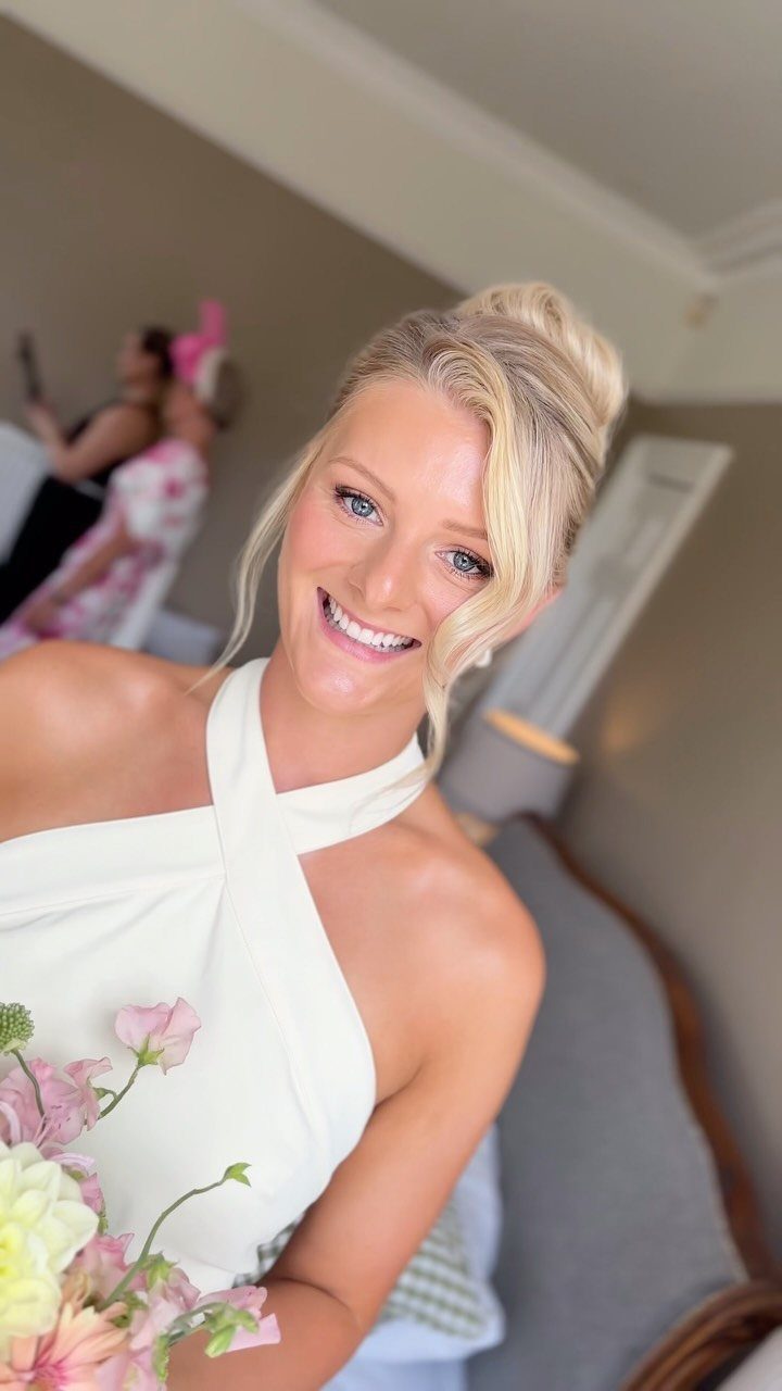 Blonde woman with elegant updo and makeup wearing a white halter dress