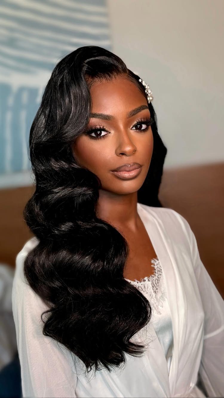 Woman with glamorous wavy black hair and full makeup wearing a white bridal robe.
