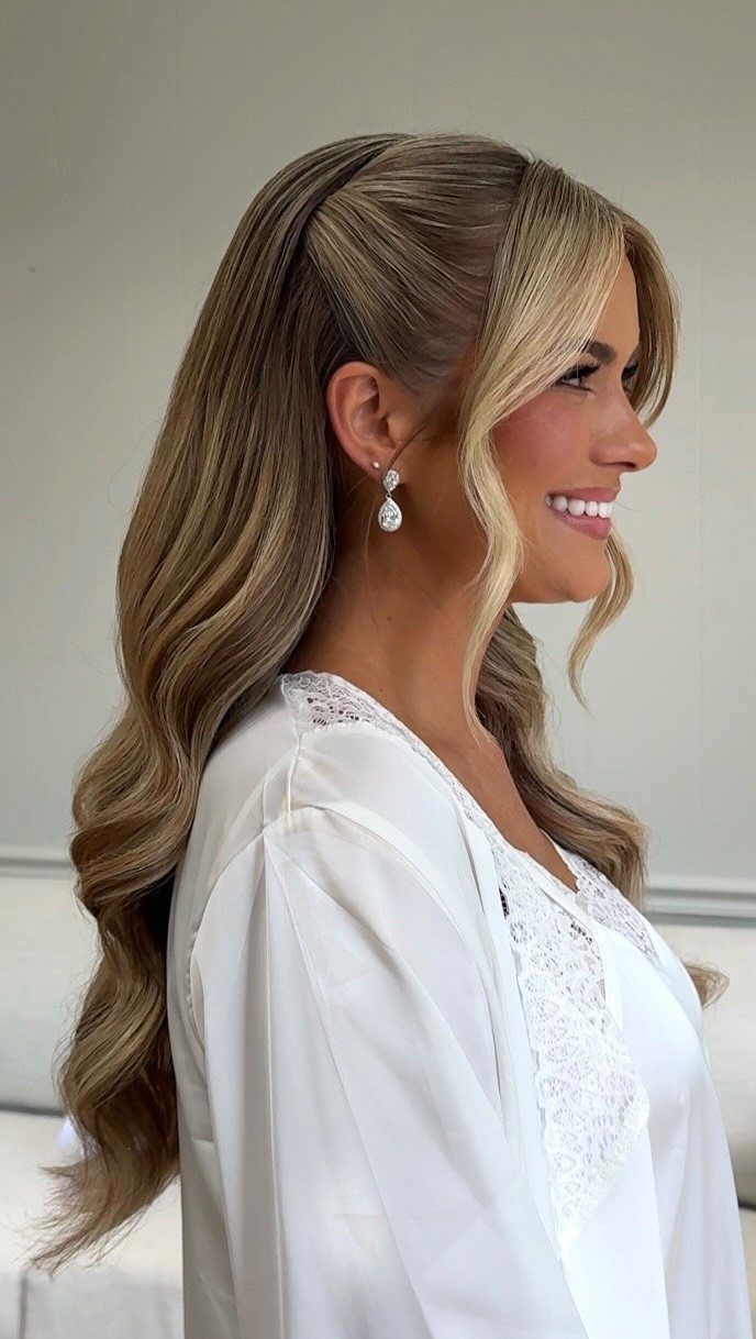 Woman with wavy blonde half-up hairstyle and bridal makeup wearing a white lace robe.