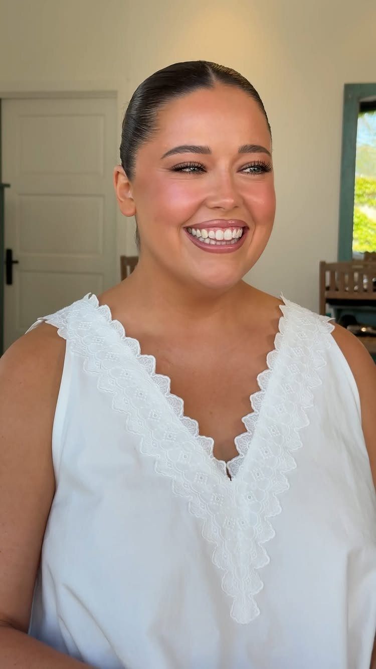 Smiling woman with polished makeup and slicked-back hair wearing a white lace top.