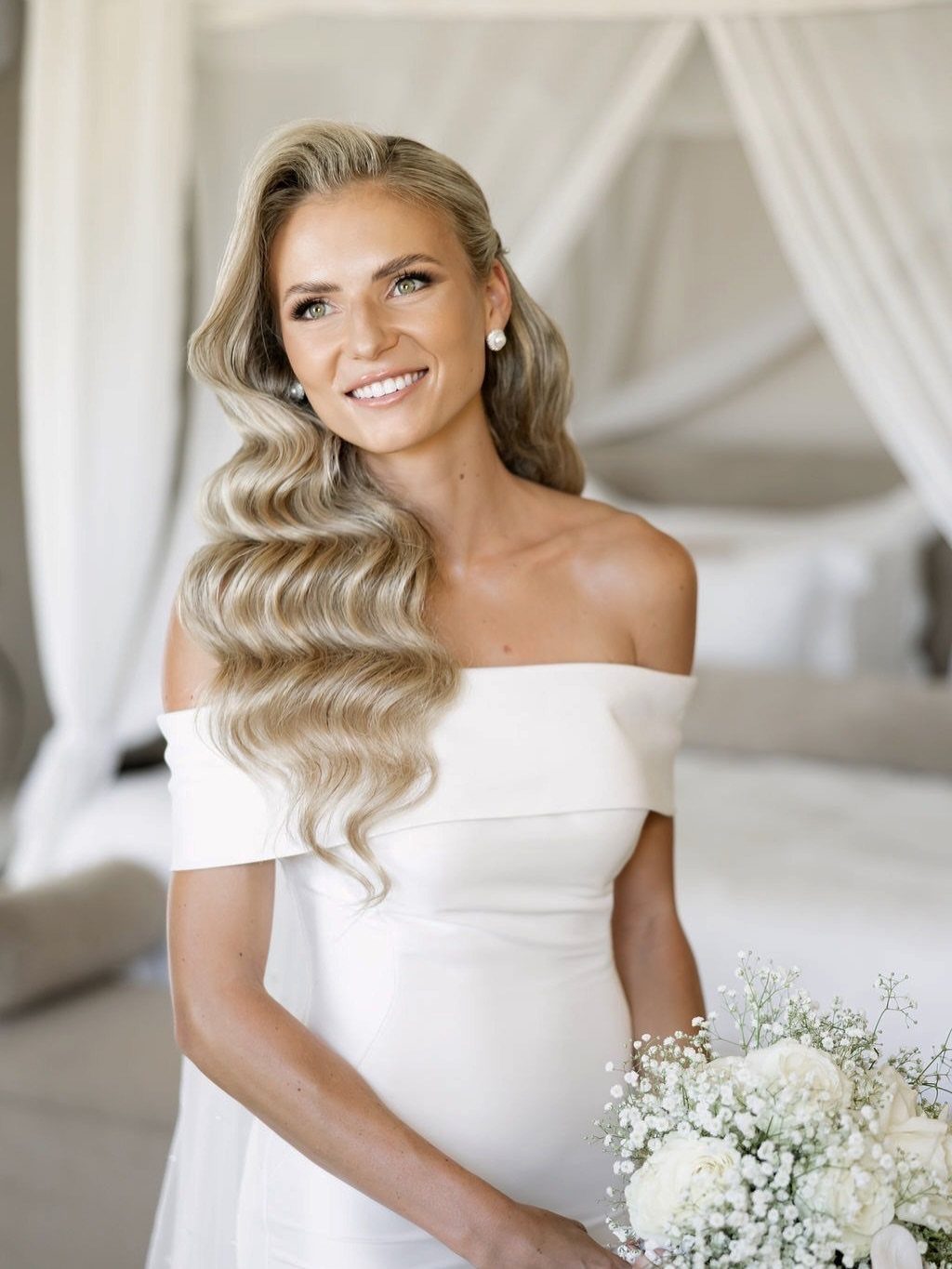 Bride with wavy blonde hair and makeup holding a white flower bouquet.