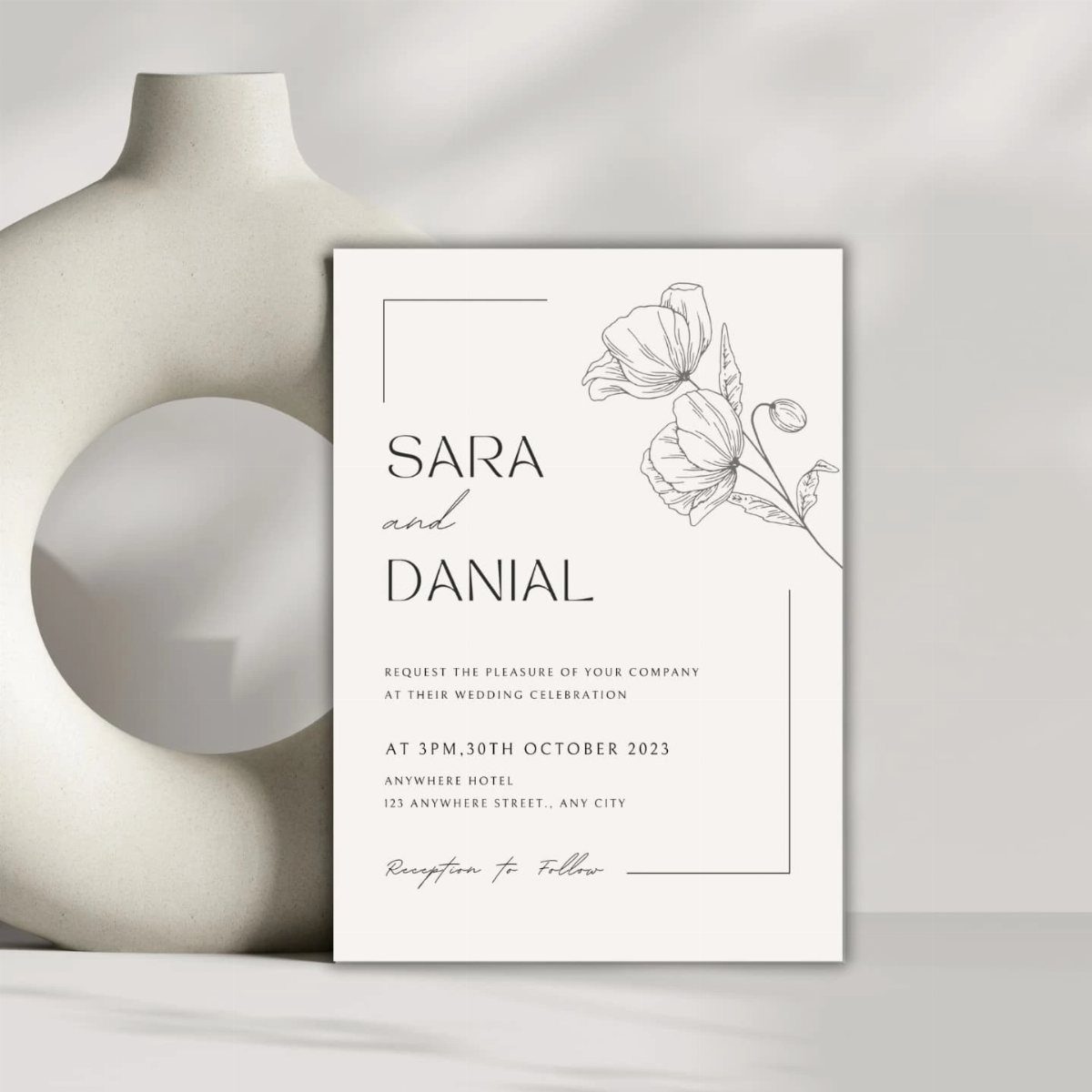 Wedding invitation card with floral line art leaning against a white sculptural vase.