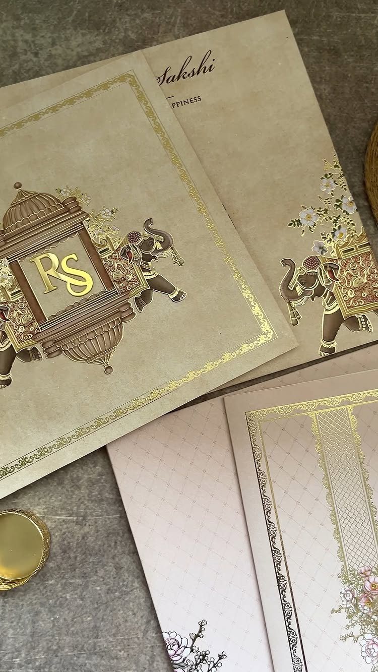Wedding invitation cards with gold foil elephants and ornate borders on grey background.