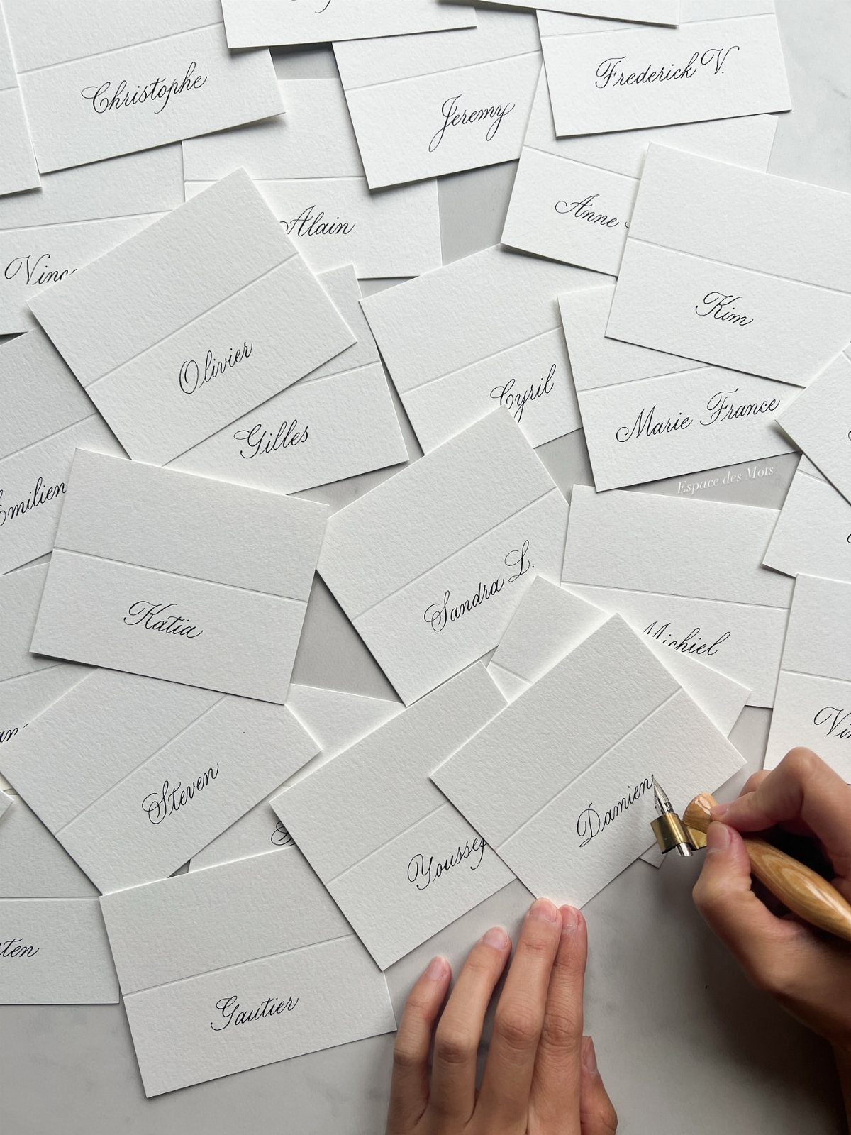 Calligraphy pen writing guest names on white folded wedding place cards