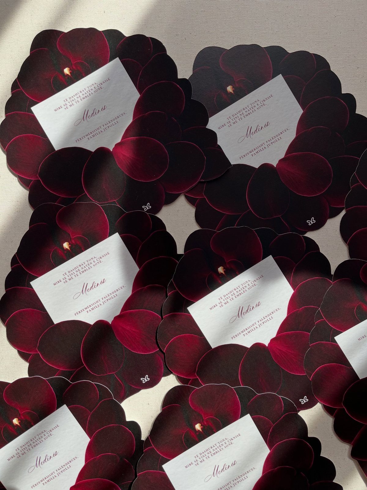 White rectangular place cards with cursive text surrounded by deep red orchid petals.