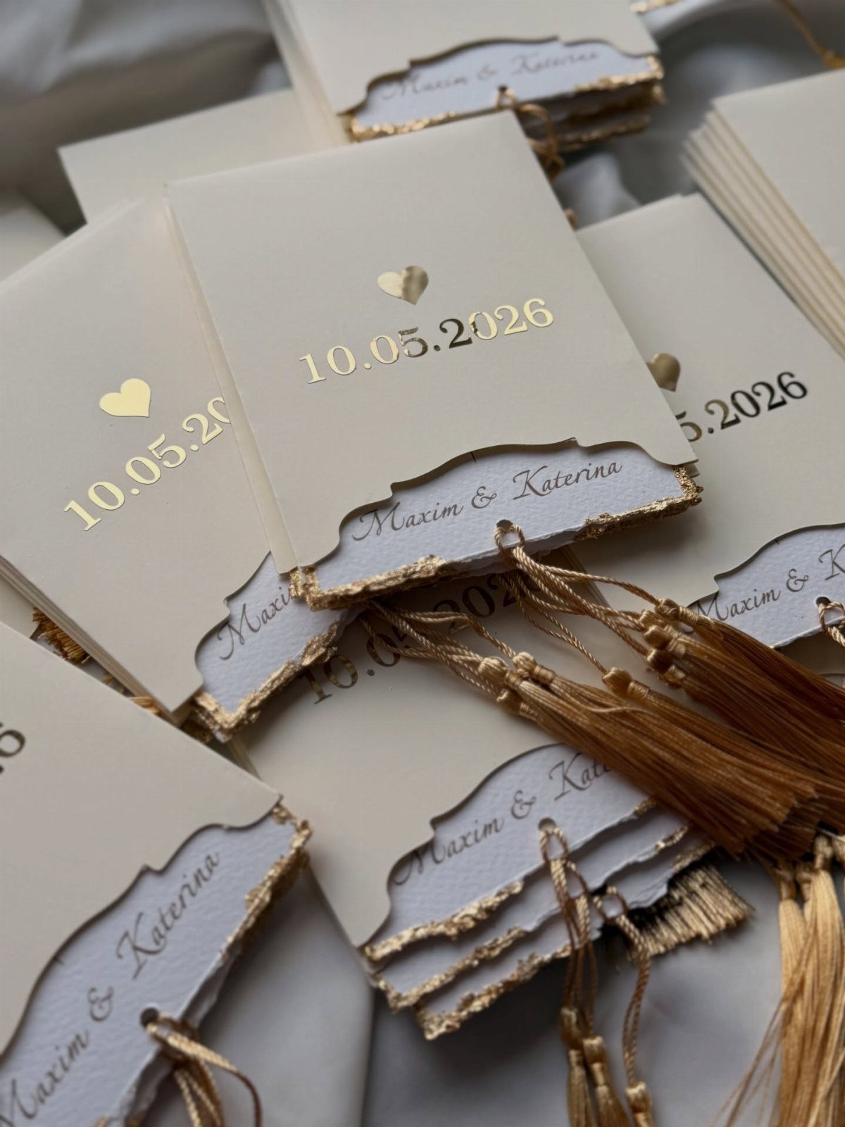 Cream wedding cards with gold foil dates and tassels on torn gilded edges.