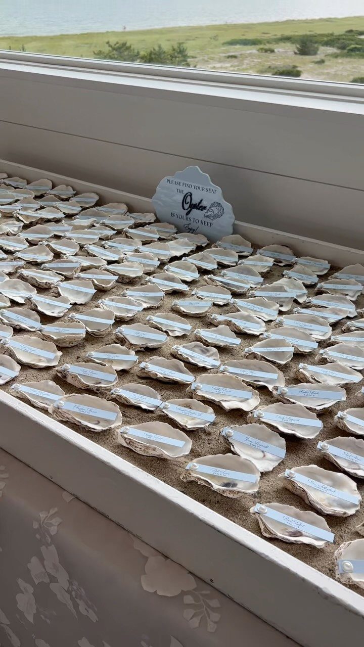 Oyster shells with name tags used as wedding place cards on a white tray.