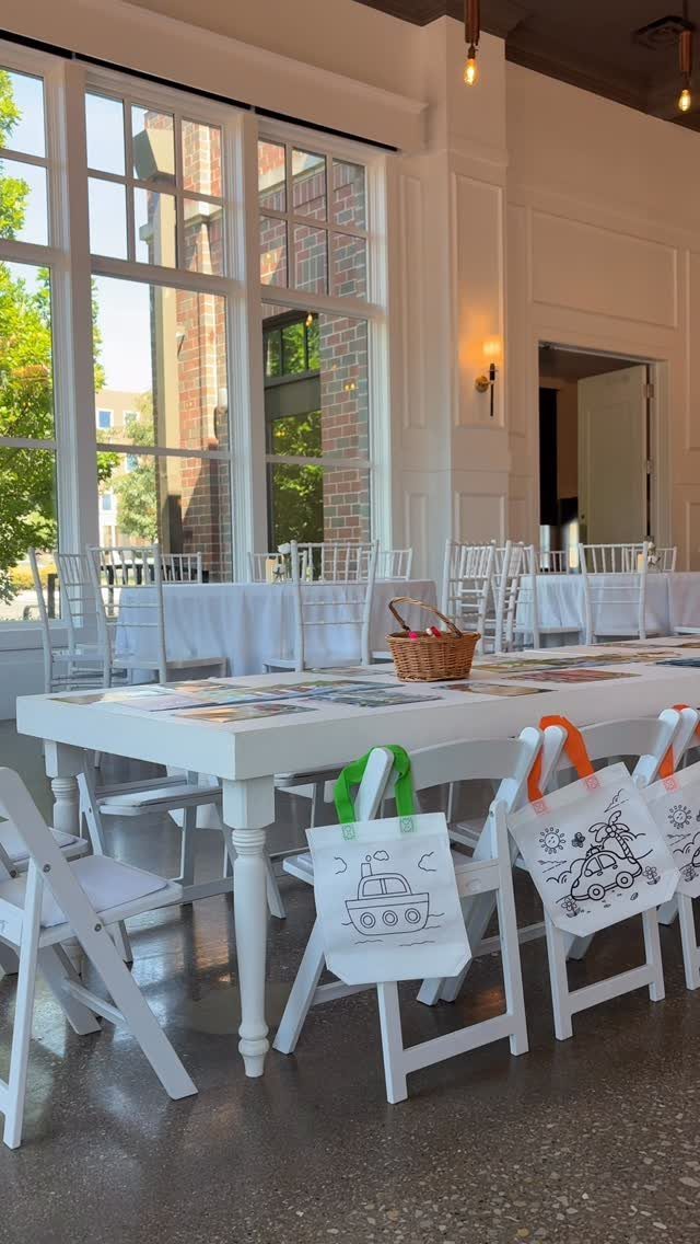 White kids table with drawing tote bags hanging from white folding chairs
